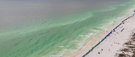 A beach with a long stretch of umbrellas and people.