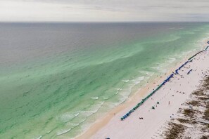 A beach with a long stretch of umbrellas and people. - Modern Bliss -Destin Condo 3 Pools & Tennis (Destin)