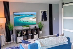 A modern living room with a flat-screen TV, a sofa, a coffee table, and decorative plants. - Modern Bliss -Destin Condo 3 Pools & Tennis (Destin)