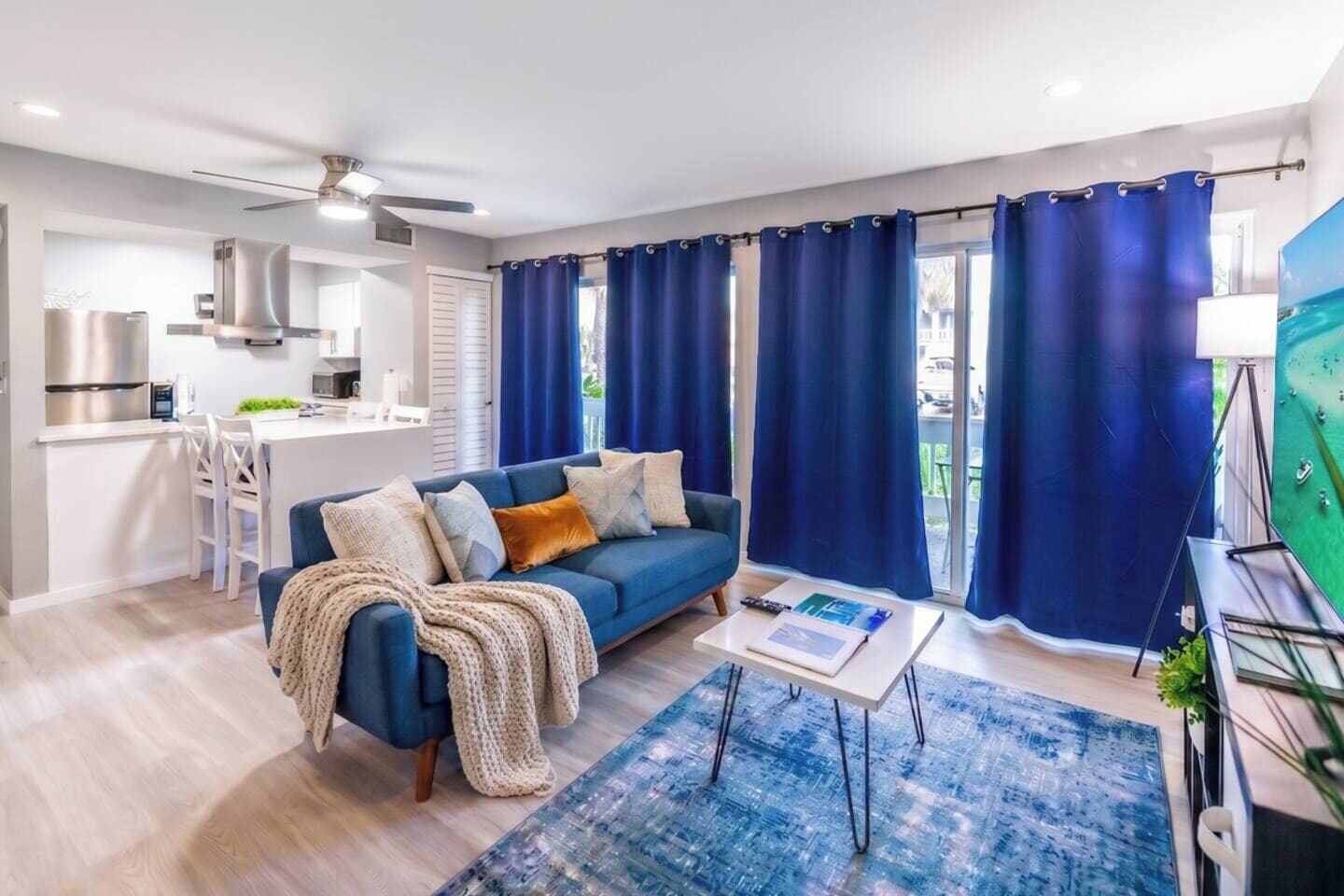 Ein modernes Wohnzimmer mit einer Couch, einem Couchtisch und Blick auf die Küche und den Balkon.