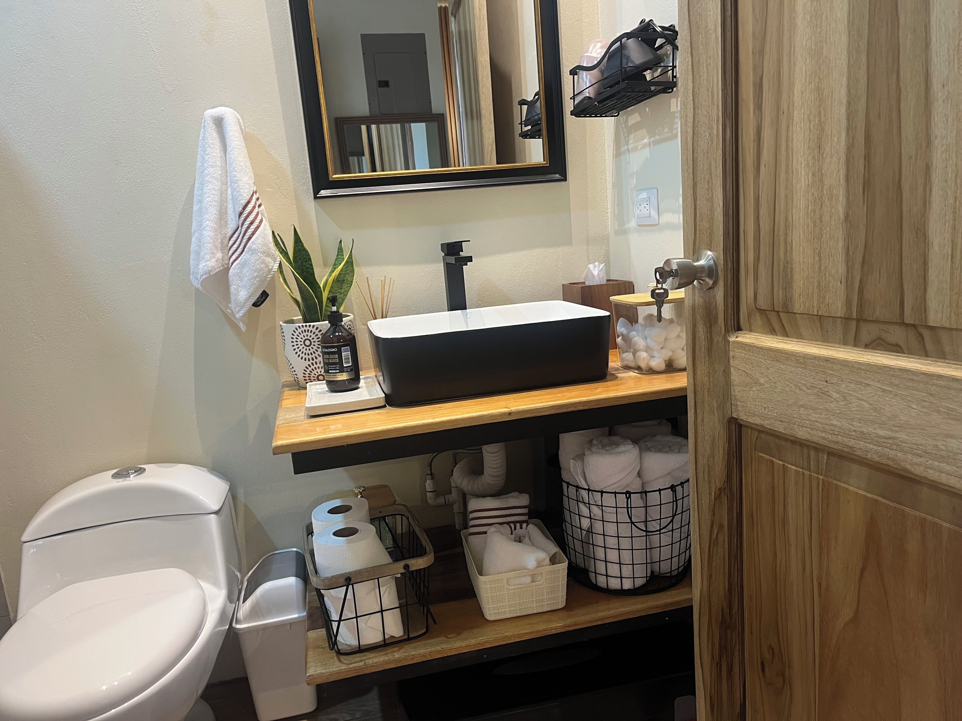 Une salle de bain équipée de toilettes, d’un lavabo, d’un miroir et d’étagères de rangement.