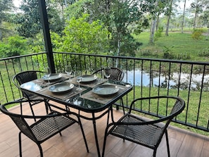 A table set for four with chairs, a railing, and a view of a pond.
