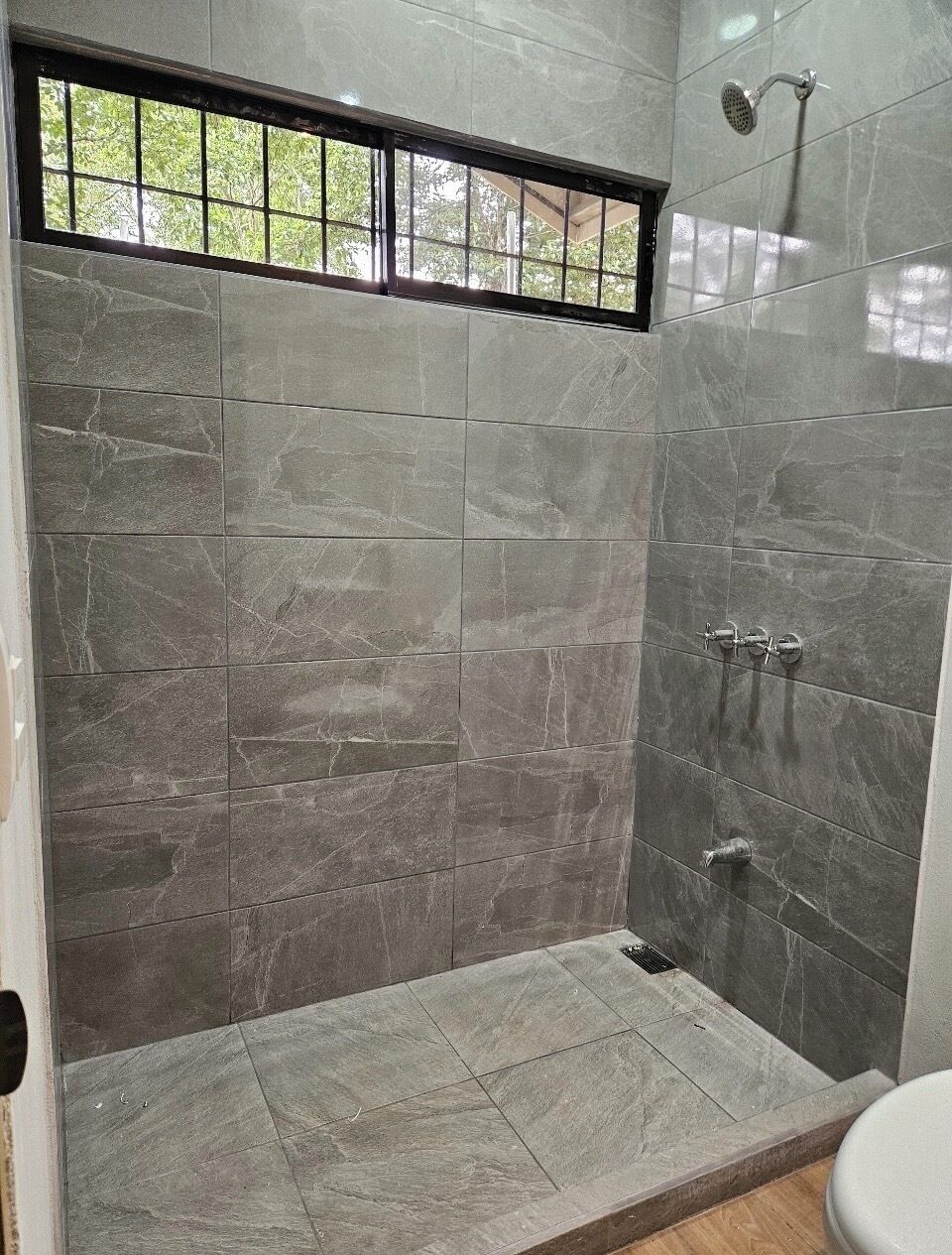 Un baño con ducha, paredes de azulejos y una ventana.