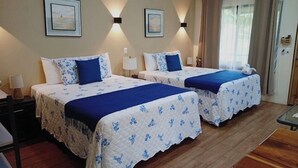A hotel room with two beds, each with a blue and white floral bedspread, a nightstand with a lamp, and a wooden floor.