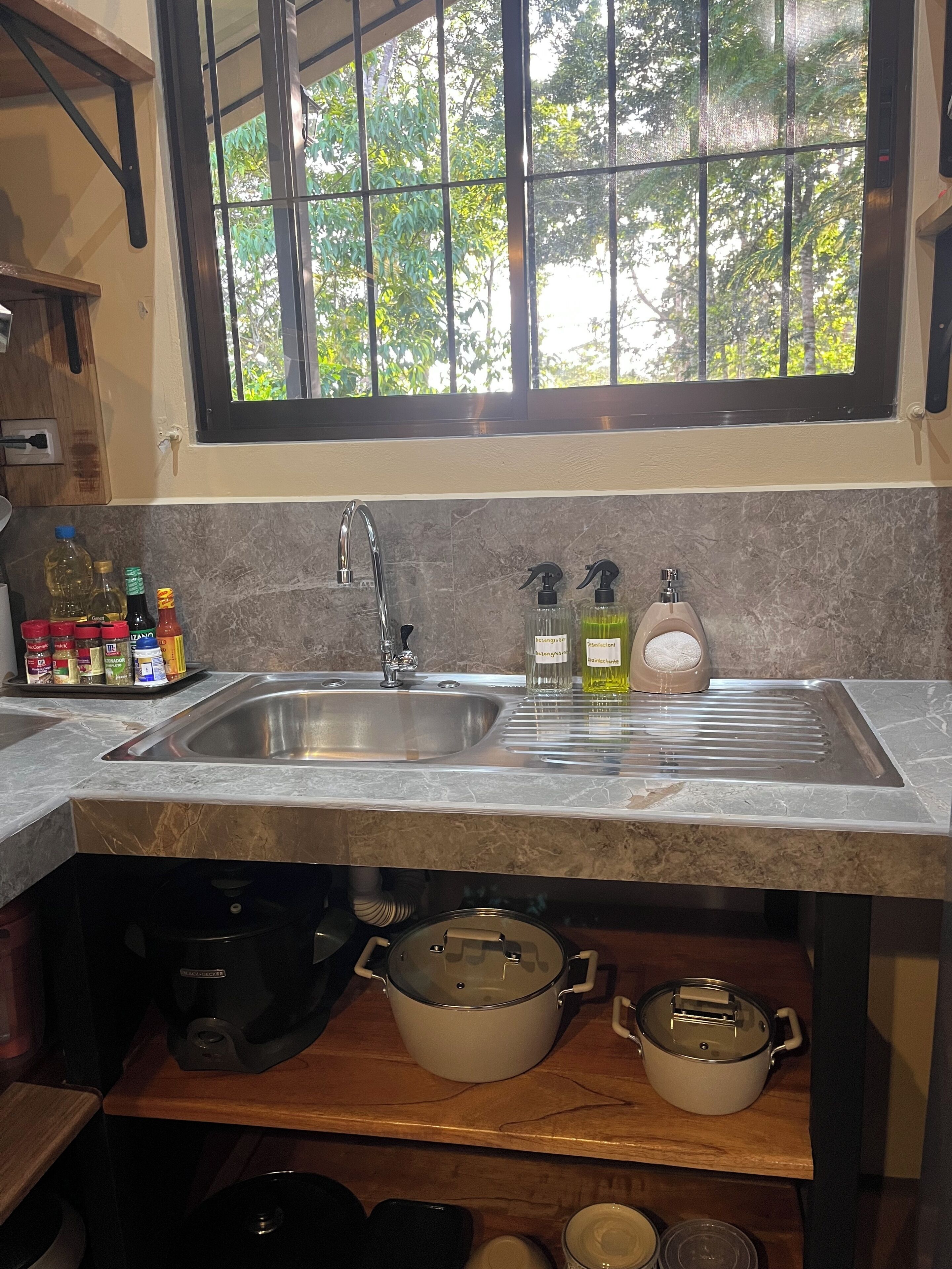 A kitchen with a stainless steel sink, a window with a view of trees, and various kitchen items on the counter.