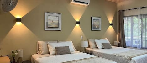 A hotel room with two beds, a ceiling fan, wall-mounted air conditioning, and framed artwork.