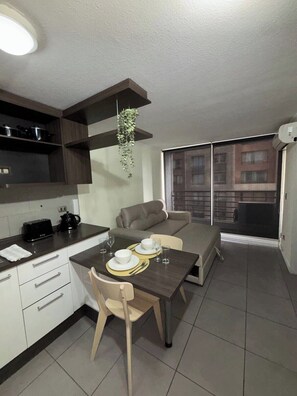 A modern kitchen with a dining area, a sofa, and a view of buildings through a large window. - "Fully equipped apartment with an elevated pool — Providencia, just steps away from everything" (Providencia)