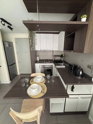 A modern kitchen with a dining table set for two, a built-in oven, and a coffee machine. - "Fully equipped apartment with an elevated pool — Providencia, just steps away from everything" (Providencia)