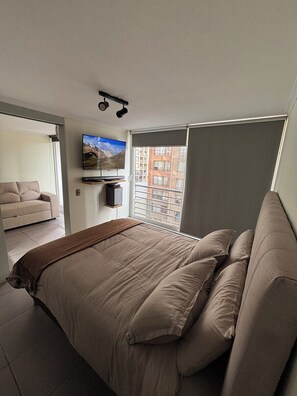 A bedroom with a bed, a TV mounted on the wall, and a window with a view of buildings. - "Fully equipped apartment with an elevated pool — Providencia, just steps away from everything" (Providencia)
