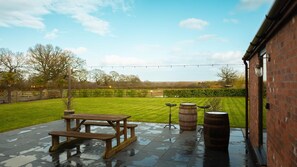 A patio with a wooden table and benches, surrounded by a brick wall and a grassy lawn. - Country Retreat, Barn with Annexe - Large enclosed garden with countryside views (Wrexham)
