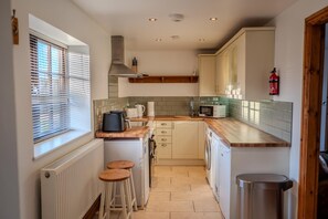 A compact kitchen with a built-in oven, a microwave, and a coffee maker. There are stools at the counter, and a radiator is visible on the left.