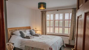 Quarto com cama de madeira, janela com persianas e luminária pendente.