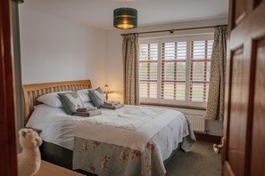 A bedroom with a wooden bed, a window with blinds, and a hanging light fixture. - Country Retreat, Barn with Annexe - Large enclosed garden with countryside views (Wrexham)