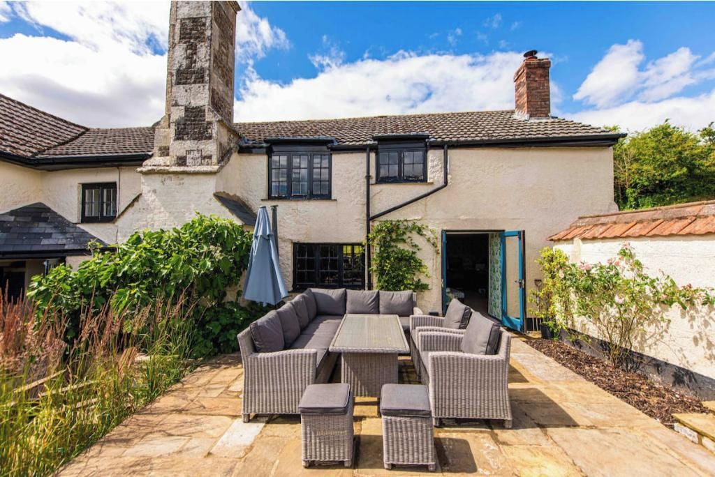 A patio with a sectional sofa and ottomans, a stone pathway, and a building with a chimney.
