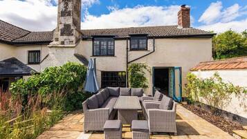 A patio with a sectional sofa and ottomans, a stone pathway, and a building with a chimney.