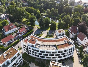 Ein modernes Gebäude mit einer gebogenen Dachterrasse, umgeben von üppiger Vegetation und einem kleinen Wasserspiegel.