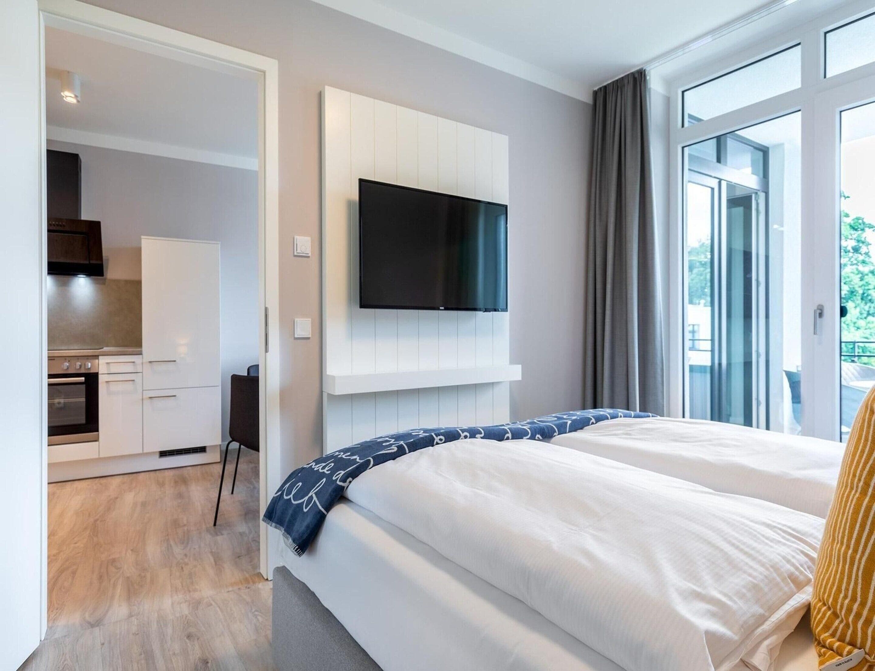 Una habitación de hotel con cama, televisión montada en la pared y vistas por la ventana.