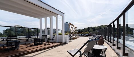 Una terraza al aire libre con mesas y sillas, un deck de madera y vistas al horizonte de la ciudad.