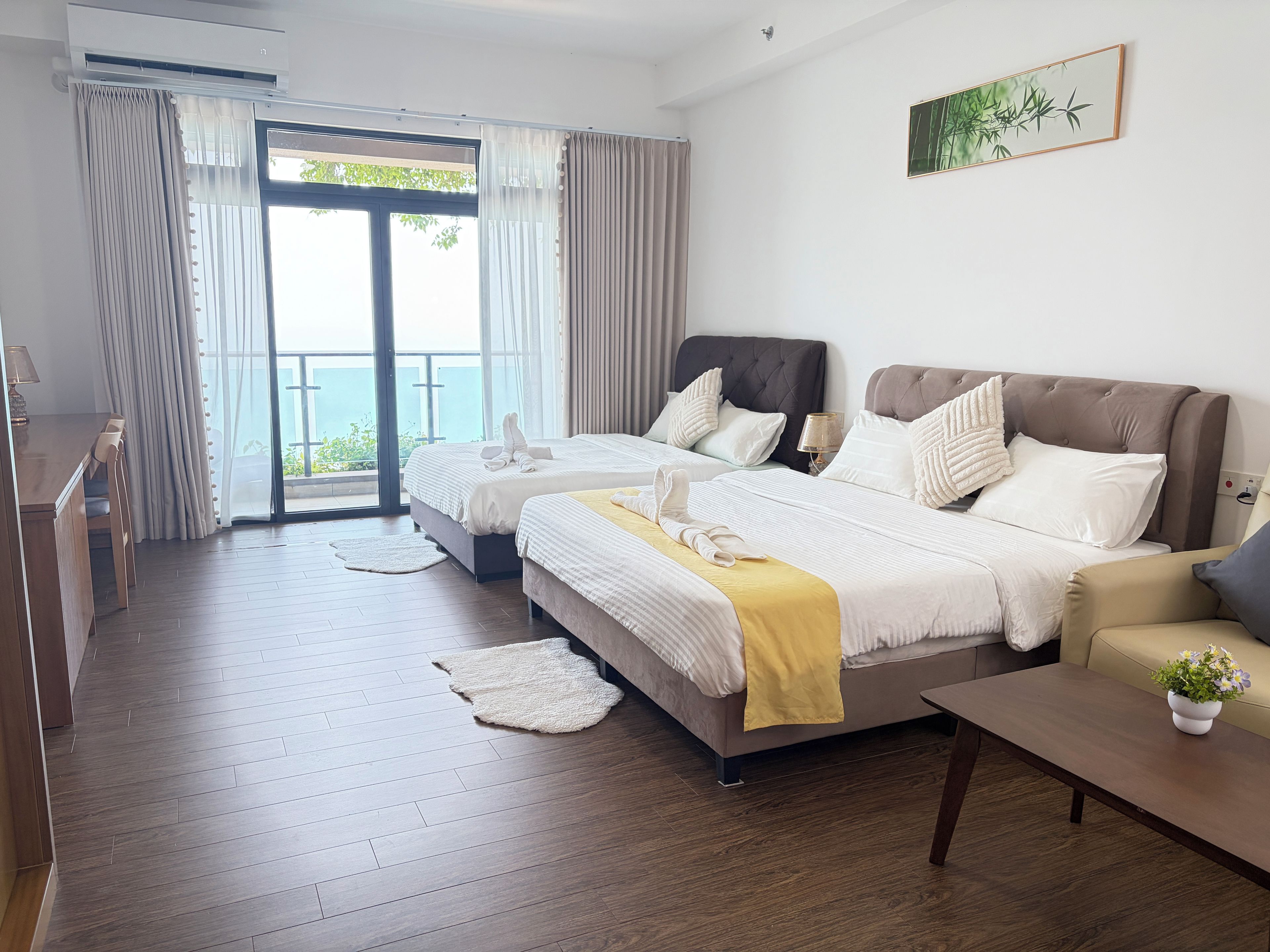 Habitación de hotel con dos camas, zona de comedor y balcón con vistas.
