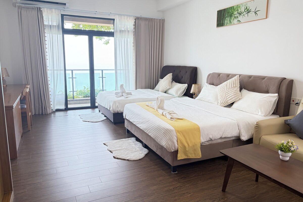 A hotel room with two beds, a dining area, and a balcony with a view.
