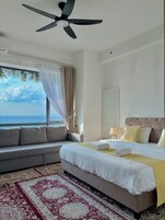 Un dormitorio con cama, sofá, ventilador de techo, ventana con cortinas y vista al mar.