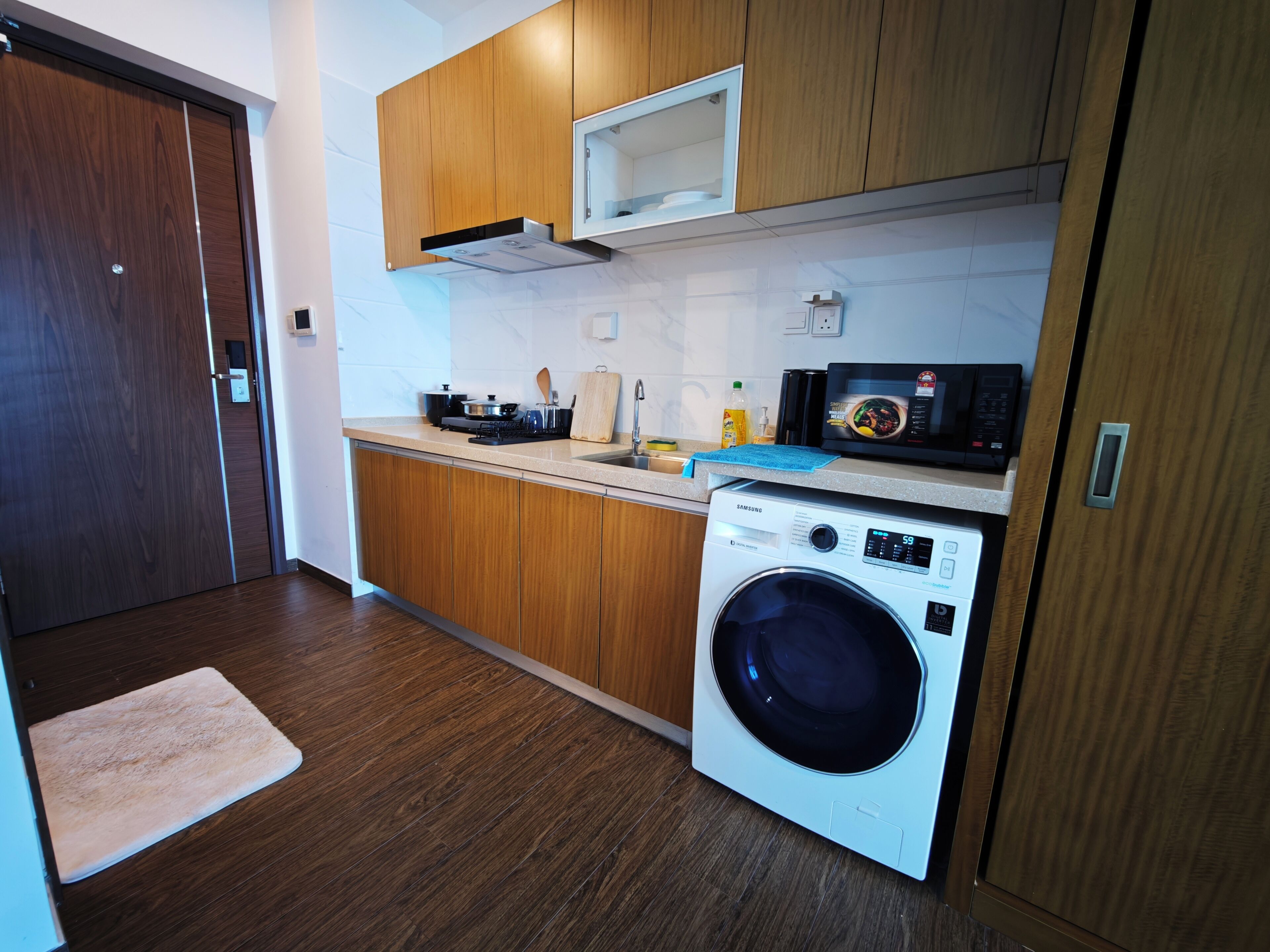Una cocina funcional con armarios de madera, lavadora, microondas y lavabo.