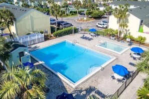 A swimming pool with a separate section, surrounded by lounge chairs and umbrellas, with palm trees and a parking area in the background. - Modern Serenity - Destin Private Beach Access (Destin)