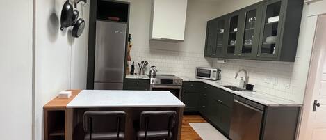 Una cocina moderna con una isla central, taburetes de bar, electrodomésticos de acero inoxidable y armarios color verde oscuro.