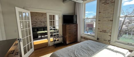 Un dormitorio con cama, cómoda, televisor y vistas al exterior.