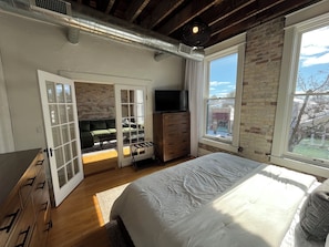 A bedroom with a bed, dresser, TV, and a view of the outdoors.