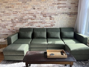 A sectional sofa with a wooden tray table in front, against a brick wall.