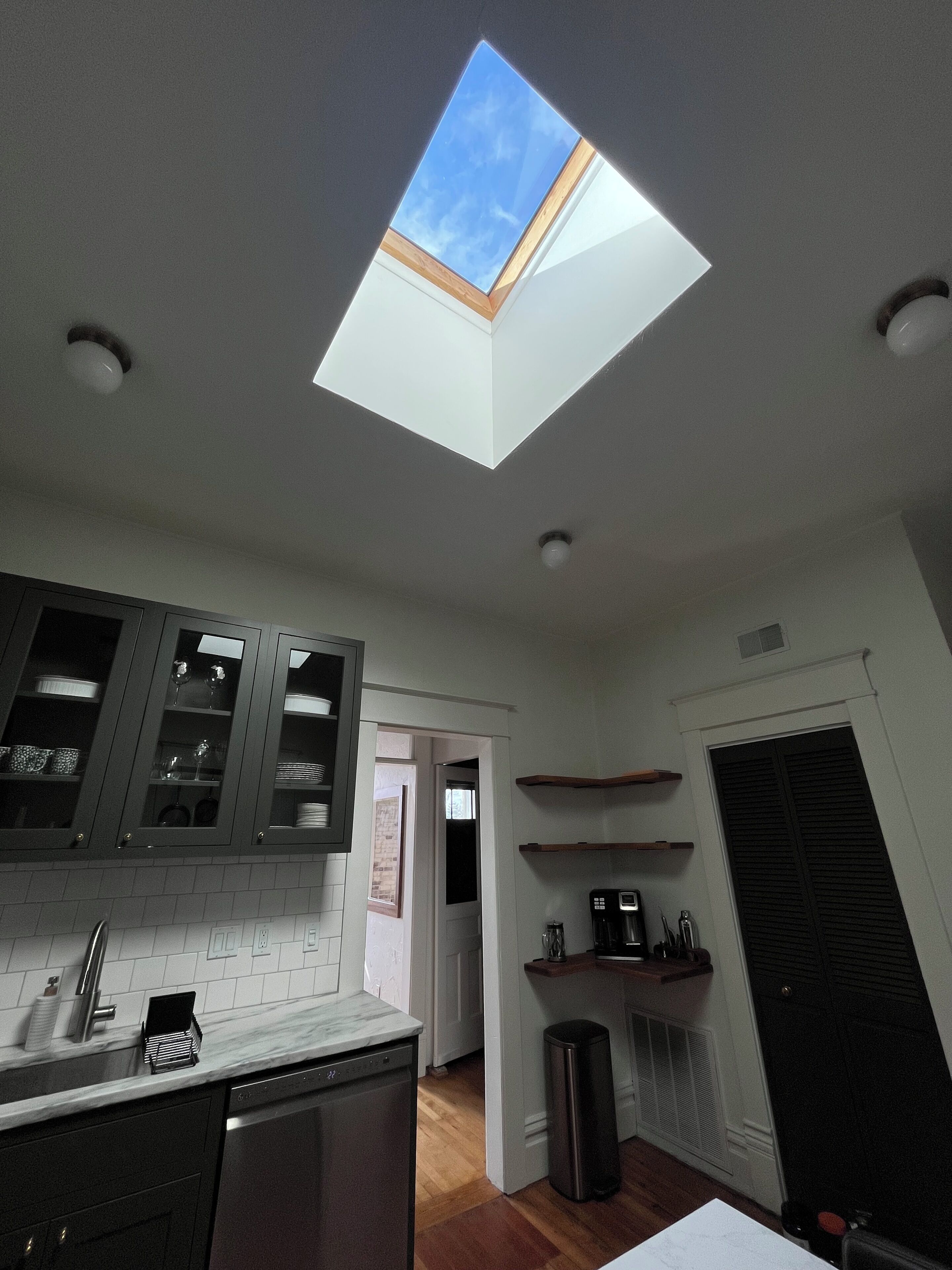 A kitchen with a skylight, wooden cabinets, a dishwasher, and a coffee machine.