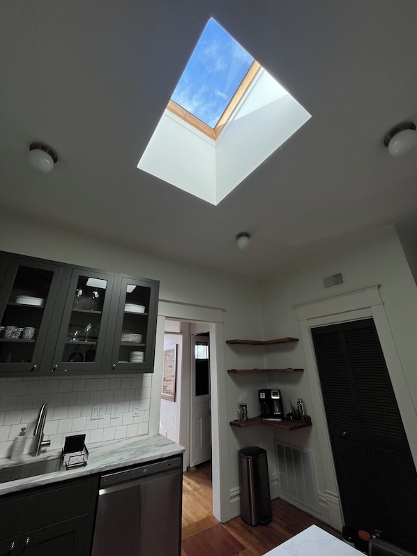 A kitchen with a skylight, wooden cabinets, a dishwasher, and a coffee machine.