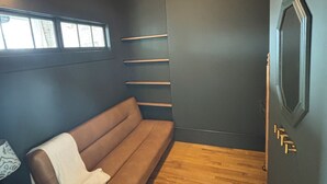 Et værelse med en brun sofa, trægulv, en vægmonteret hylde og en enkelt lysarmatur.