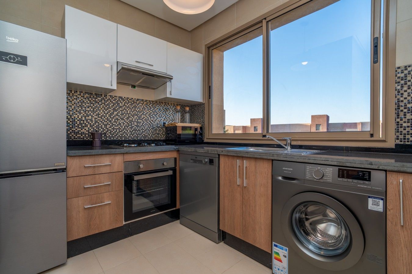 A modern kitchen with a built-in washer, a large window, and a tiled backsplash.