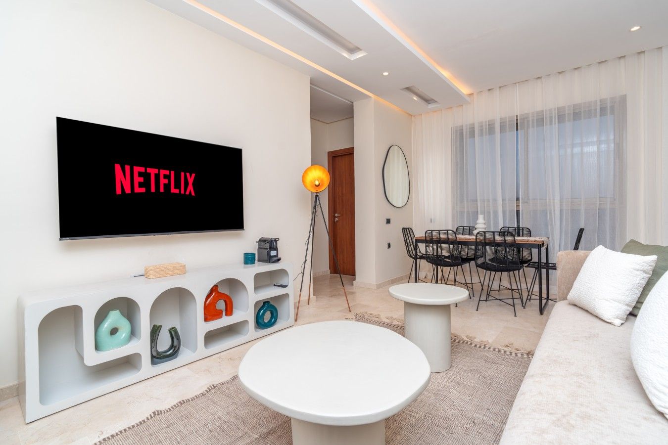 A modern living room with a flat-screen TV displaying 'NETFLIX,' a dining area with a table and chairs, and a sofa.