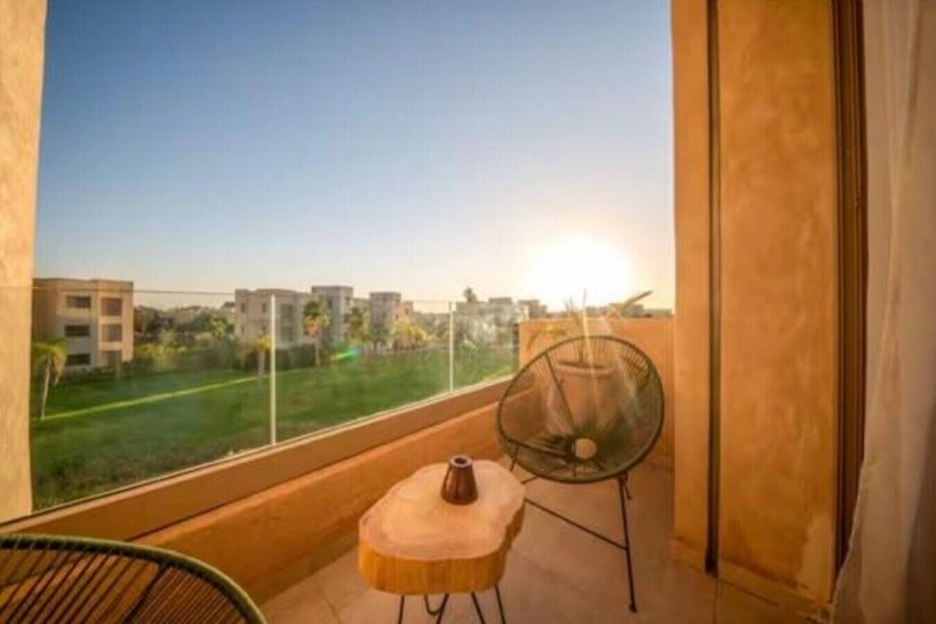Un balcon avec vue sur des immeubles et un espace verdoyant. On y trouve une chaise et une petite table sur laquelle est posé un vase.