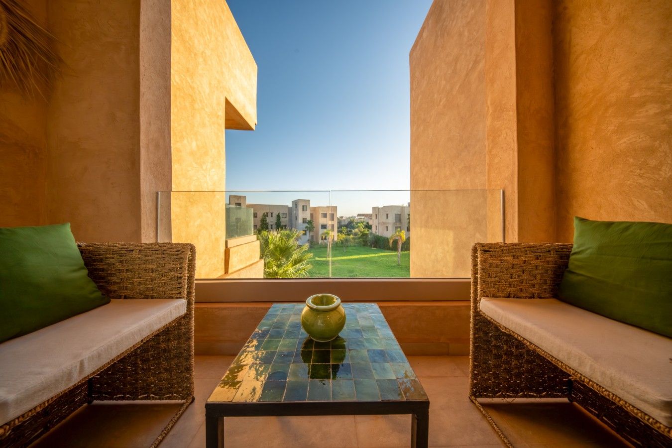 A balcony with wicker furniture and a tiled table, overlooking a residential area.