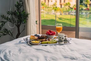 A breakfast tray on a bed with a window view of a green landscape and buildings. - Prestigia Golf |Luxury 3BR| Pool&Atlas view (Marrakesh)