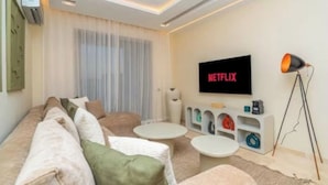 A modern living room with a sofa, two coffee tables, a TV mounted on the wall, and a lamp. - Prestigia Golf |Luxury 3BR| Pool&Atlas view (Marrakesh)