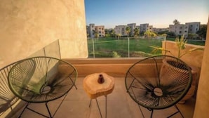 A balcony with two chairs and a small table, overlooking a residential area with buildings and greenery. - Prestigia Golf |Luxury 3BR| Pool&Atlas view (Marrakesh)