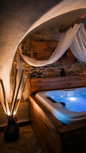 A stone-walled room with a wooden bathtub and white drapes.