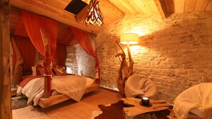 A rustic room with two beds, a stone wall, a wooden ceiling, and a lamp.