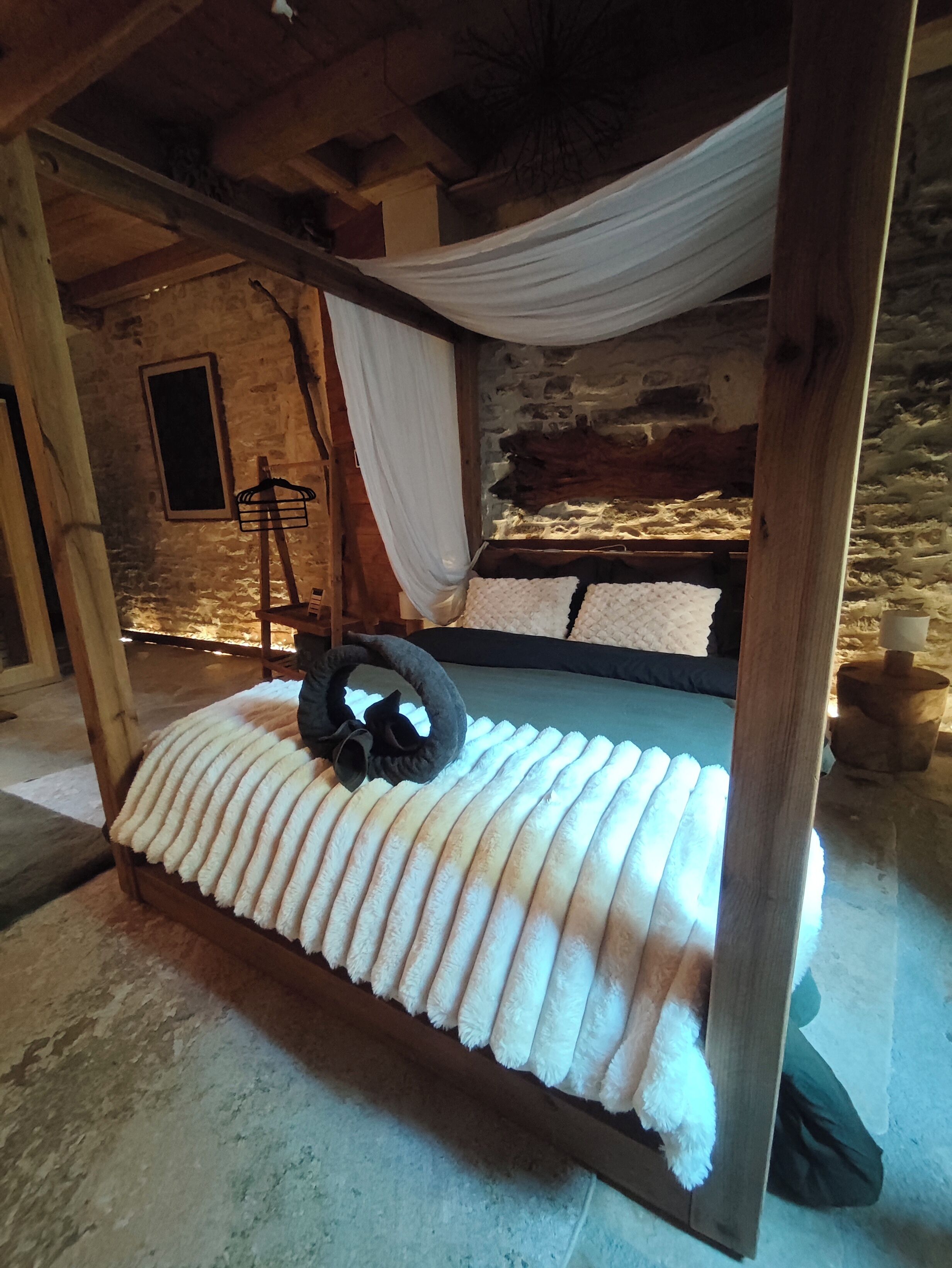 Ein rustikales Holzbett mit weißem Baldachin, eine Steinwand und ein kleiner Holzschemel.