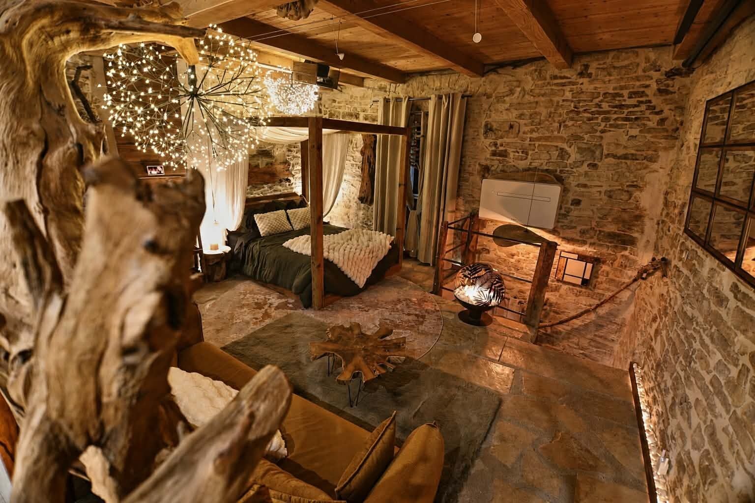 Una stanza rustica con una parete in pietra, un letto a baldacchino, un tavolo di legno e un lampadario particolare.
