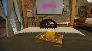 Ett mysigt rum med en säng, ett träbricka med popcorn och en skärm som visar ”NETFLIX”.