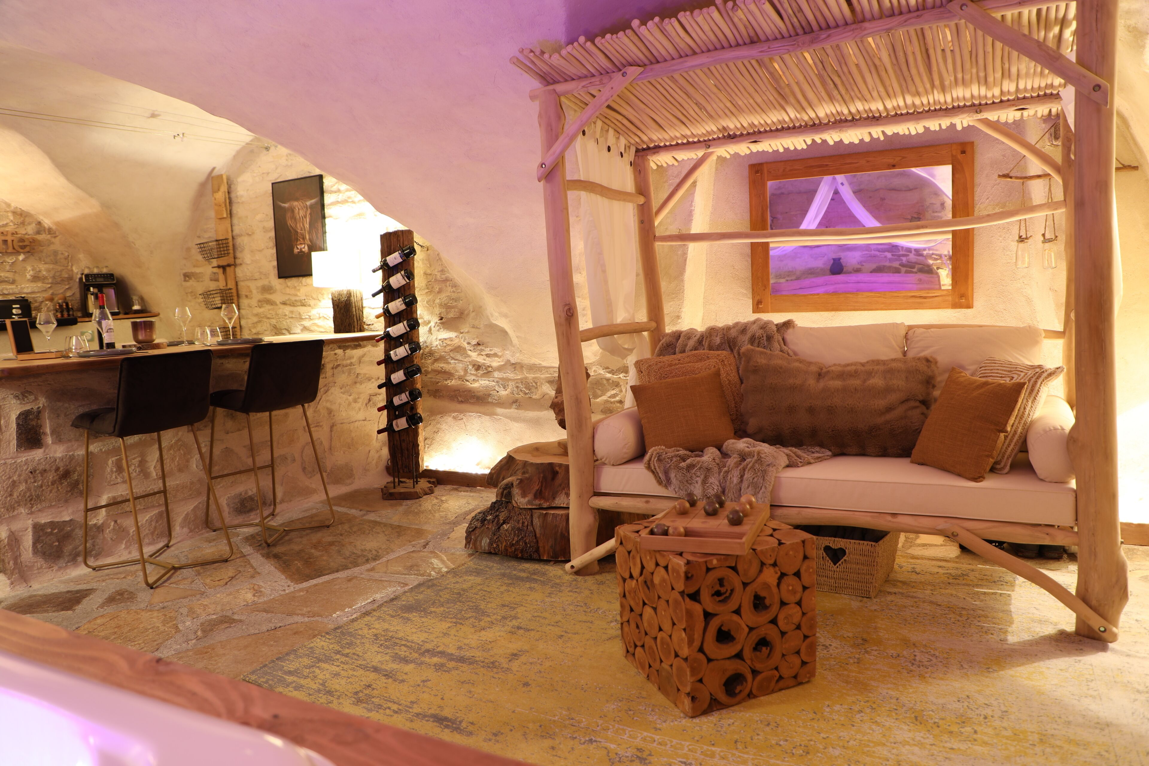 A cozy room with a stone wall, a wooden bar, a cushioned seating area, and a hanging light fixture.