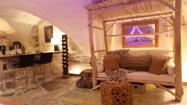 A cozy room with a stone wall, a wooden bar, a cushioned seating area, and a hanging light fixture.