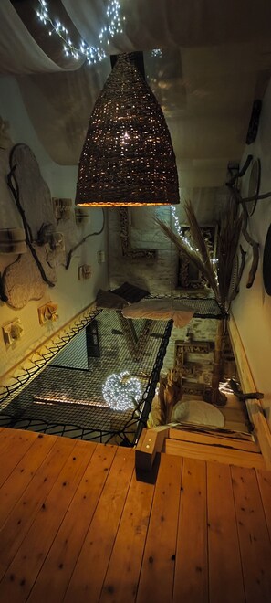 Quarto com piso de madeira, luminária pendente e parede com detalhes decorativos.
