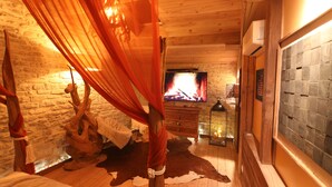 A cozy room with a wooden floor, a stone wall, a fireplace, and a bed with a canopy.